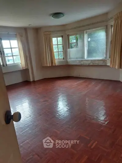 Spacious empty room with wooden flooring and large windows, perfect for customization.