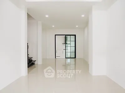 Spacious modern living room with glossy tiled floors and glass door leading to kitchen.