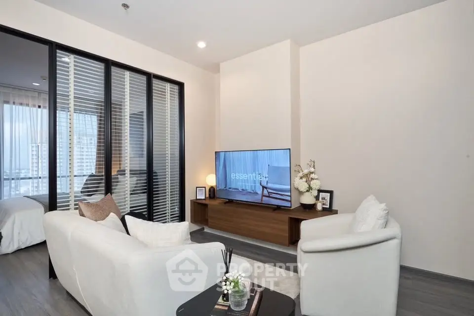 Modern living room with sleek furniture and large TV, adjacent to a cozy bedroom with city view.