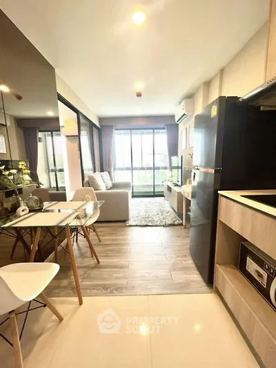 Modern open-plan living room with kitchen, featuring sleek furniture and large windows.