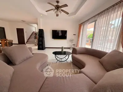 Spacious living room with modern curved sofa and wall-mounted TV, featuring large windows and elegant decor.