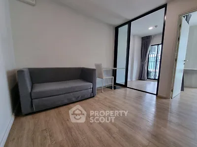 Modern living room with sleek gray sofa and glass partition leading to balcony.