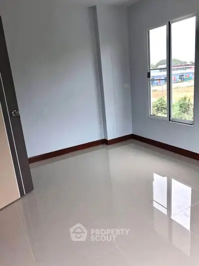 Spacious empty room with glossy tiled floor and large window offering natural light and outdoor view.