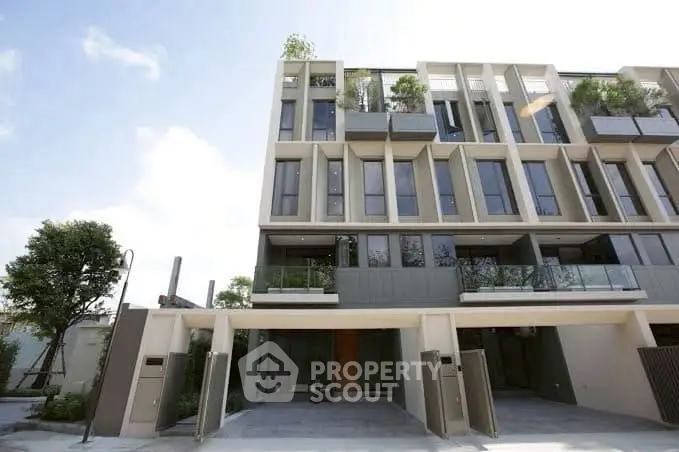Modern multi-story townhouse with large windows and balconies, showcasing contemporary architecture and lush greenery.