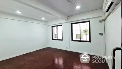 Spacious and well-lit corner unit with polished brown flooring and white walls, featuring large windows and modern air conditioning.