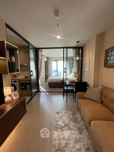 Modern open-plan living room with cozy sofa and stylish decor leading to a bright bedroom with glass partition.