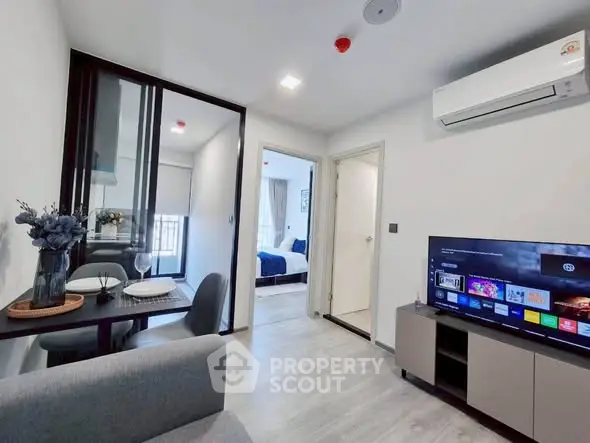 Modern living room with dining area and view into bedroom, featuring sleek furniture and air conditioning.