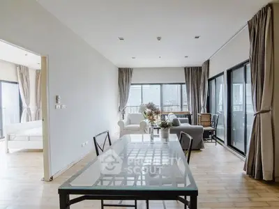 Spacious modern living room with glass dining table and large windows offering natural light.