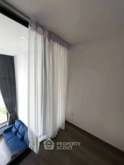 Modern living room with floor-to-ceiling windows and elegant curtains, featuring a cozy blue sofa.