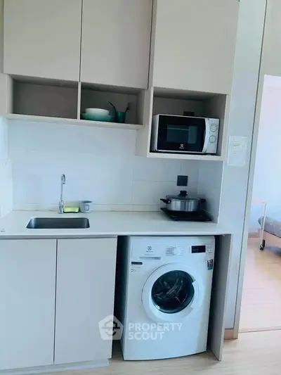 Modern compact kitchen with washing machine and microwave in a sleek apartment.