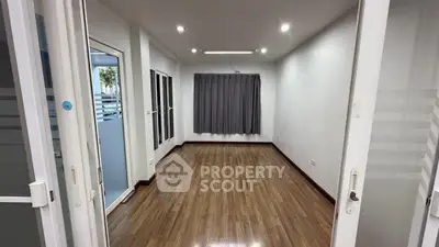 Spacious empty room with wooden flooring and large windows, perfect for customization.