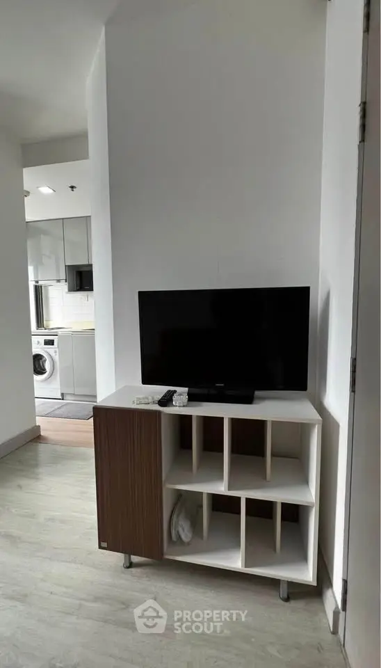 Modern apartment interior with TV stand and glimpse of kitchen featuring washing machine.