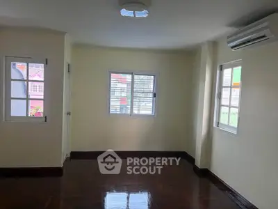 Spacious room with polished wooden floors and air conditioning, featuring large windows for natural light.