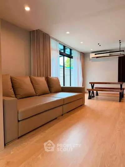 Spacious living room with modern sofa and dining table, featuring large windows and elegant lighting.