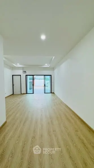 Spacious empty living room with wooden flooring and large windows for natural light.