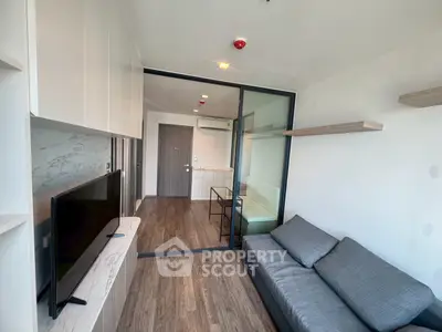 Modern living room with sleek design and glass partition, featuring a cozy gray sofa and wall-mounted TV.