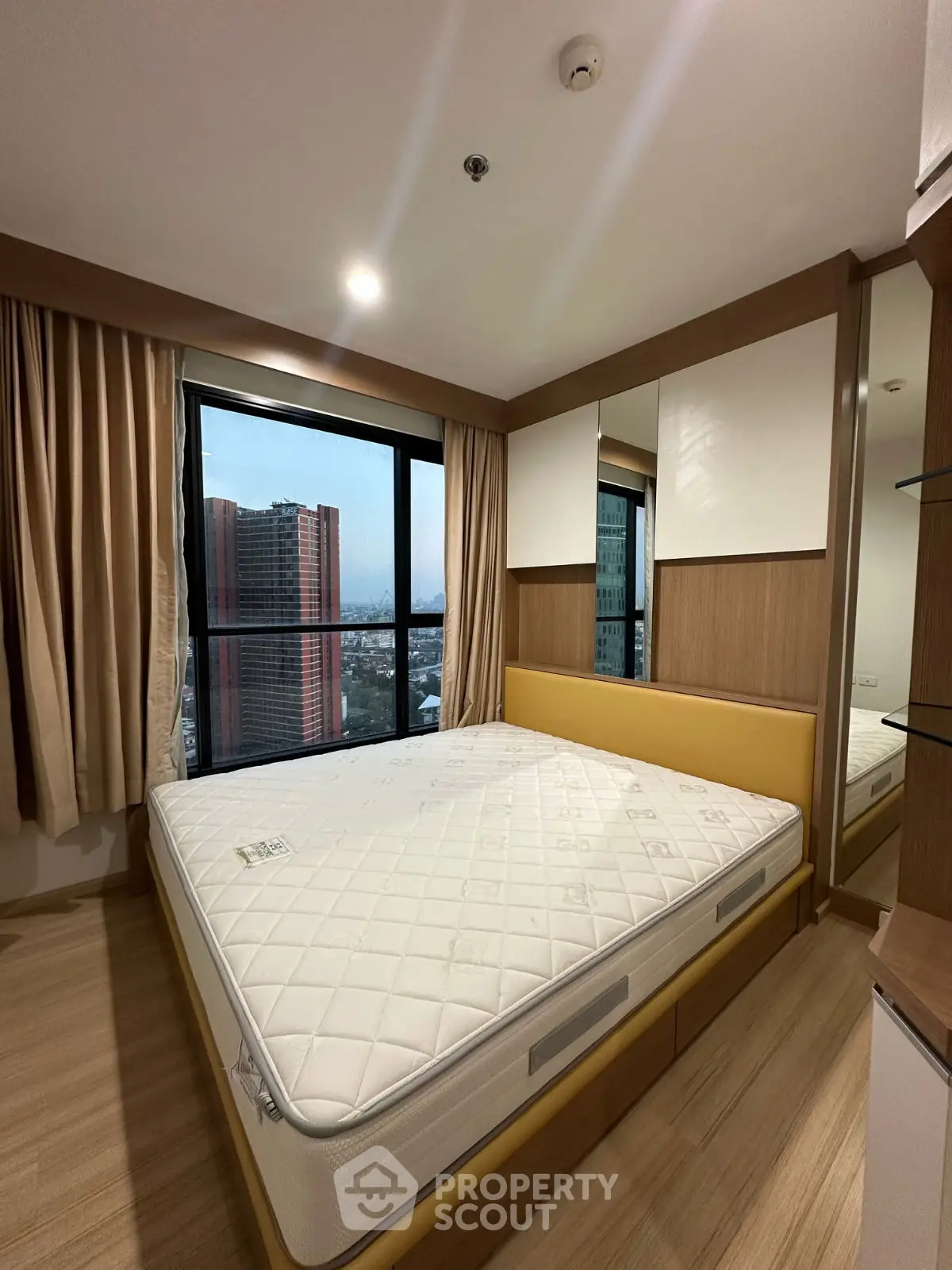 Modern bedroom with large window offering city view, featuring a comfortable bed and stylish wooden decor.