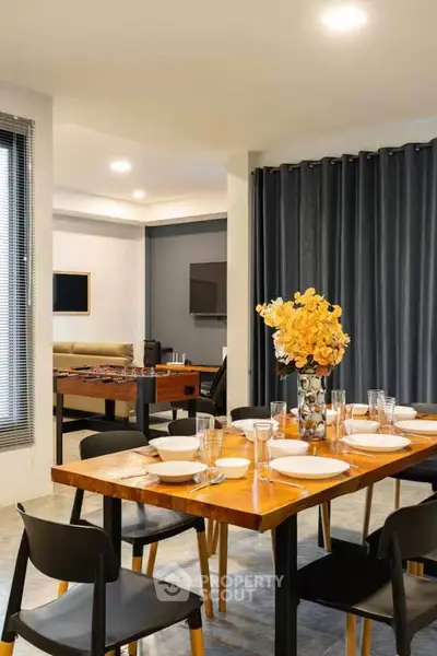 Modern dining area with stylish wooden table and chairs, adjacent to a cozy living room with entertainment setup.