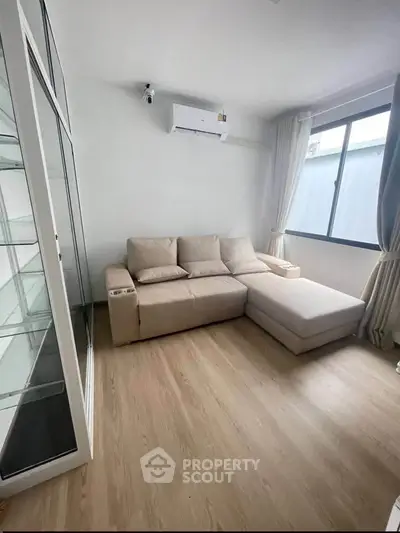 Modern living room with beige sofa and large window, featuring sleek wooden flooring.