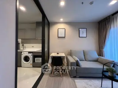 Modern living room with open kitchen and washing machine, featuring cozy sofa and dining area.