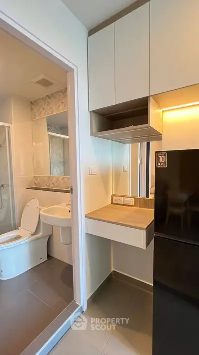 Modern apartment interior with compact bathroom and sleek kitchen area featuring a black fridge.