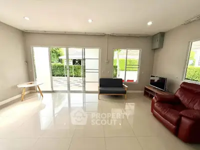 Spacious living room with modern furniture and large windows offering natural light and garden view.