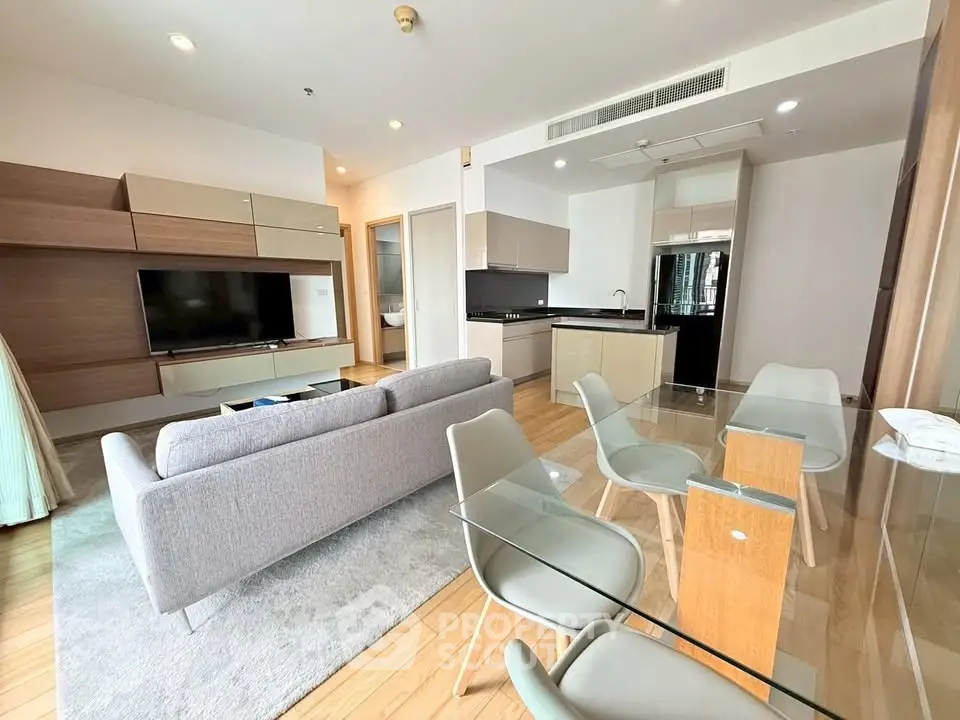 Modern open-plan living room with sleek kitchen and dining area, featuring stylish furniture and natural light.