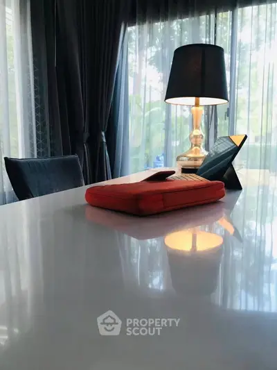 Elegant dining area with modern table, stylish lamp, and lush garden view through large windows.