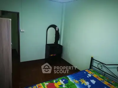 Cozy bedroom with colorful bedding and wooden flooring, featuring a small dresser and mirror.