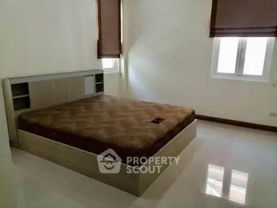 Spacious bedroom with modern bed and natural light from two windows.