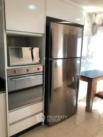Modern kitchen with stainless steel fridge and built-in oven, sleek white cabinetry, and natural light.