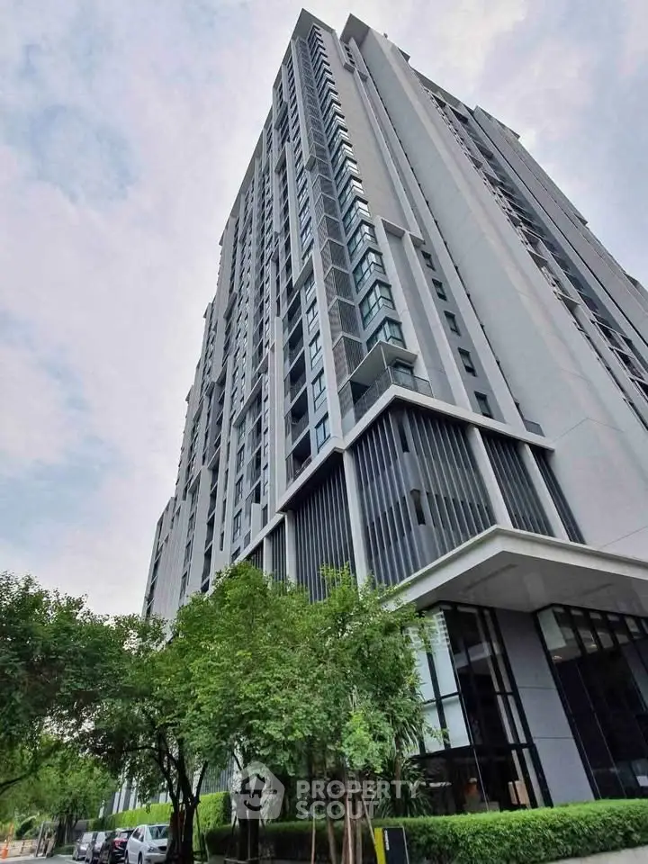 Modern high-rise building with sleek design and lush greenery at the base, offering urban living with style.