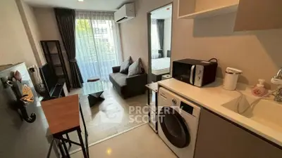 Modern studio apartment with compact kitchen and cozy living area, featuring a washing machine and microwave.