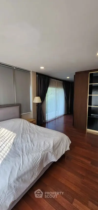 Spacious bedroom with wooden flooring and large windows for natural light