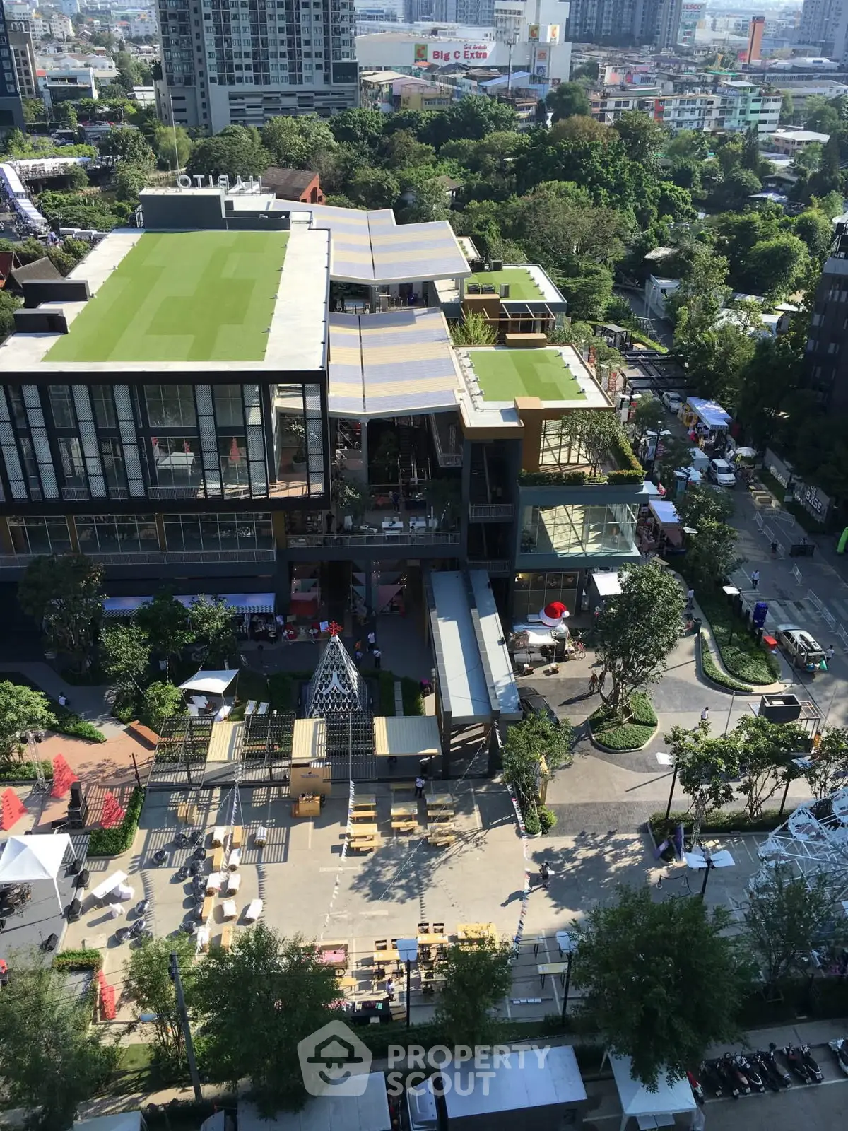 Aerial view of modern commercial building with rooftop gardens and urban surroundings.