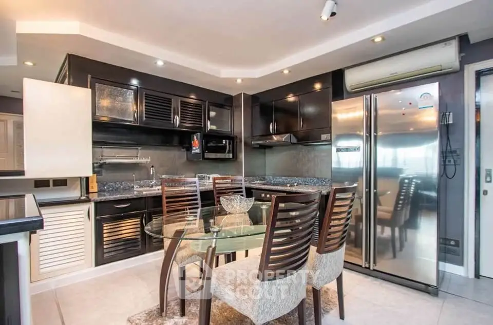 Modern kitchen with sleek black cabinets and stainless steel appliances, featuring a glass dining table and elegant chairs.