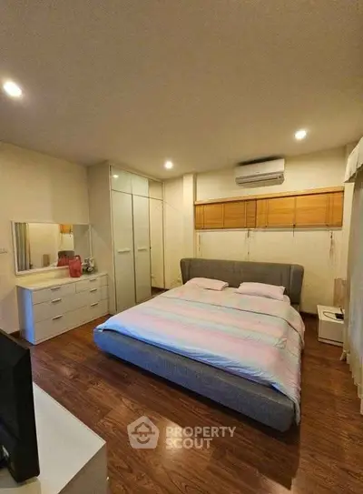 Spacious bedroom with modern decor and wooden flooring, featuring a cozy bed and ample storage.