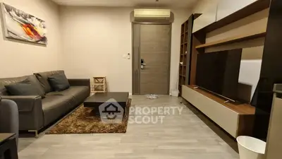 Modern living room with sleek furniture and stylish decor, featuring a large TV and air conditioning unit.