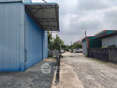 Industrial warehouse exterior with spacious driveway and metal siding, ideal for storage or manufacturing.
