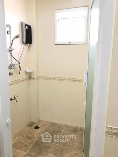 Compact bathroom with shower and tiled floor, featuring neutral tones and a small window for natural light.