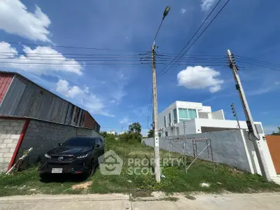 Vacant land plot with potential for development, adjacent to modern white building under clear blue sky.