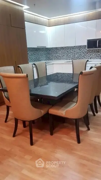 Elegant dining area with modern kitchen featuring mosaic backsplash and sleek cabinetry.