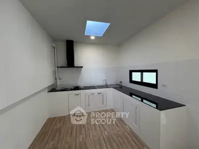 Modern kitchen with sleek black countertops and skylight, featuring a gas stove and minimalist design.