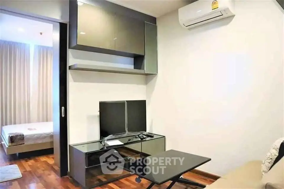 Modern living room with sleek furniture and wall-mounted TV, adjacent to a cozy bedroom.