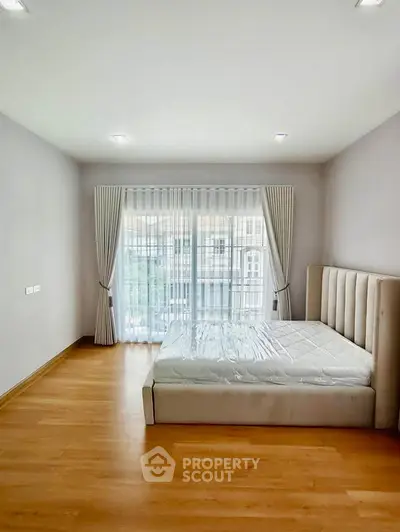 Spacious bedroom with large window and elegant curtains, featuring a modern bed and wooden flooring.