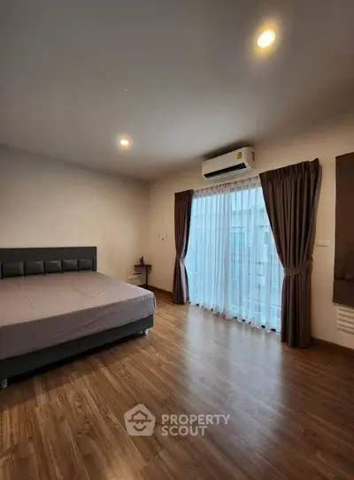 Spacious bedroom with wooden flooring and large window for natural light