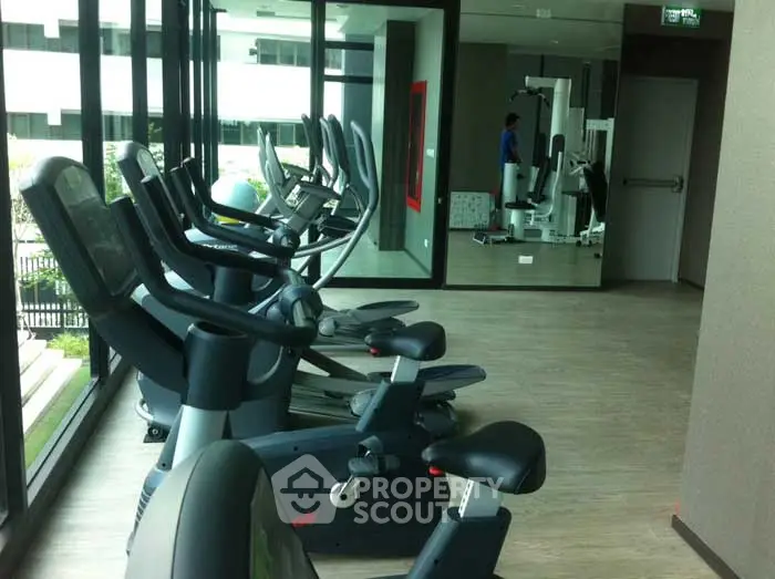 Modern gym with exercise equipment and large windows in a real estate property.