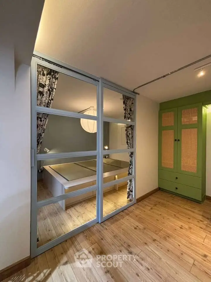 Stylish bedroom with glass partition and wooden flooring, featuring modern decor and ample natural light.