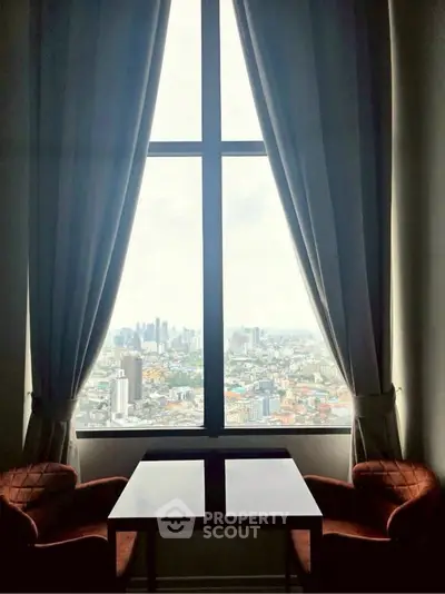 Stunning city view from a high-rise apartment window with elegant curtains and cozy seating.