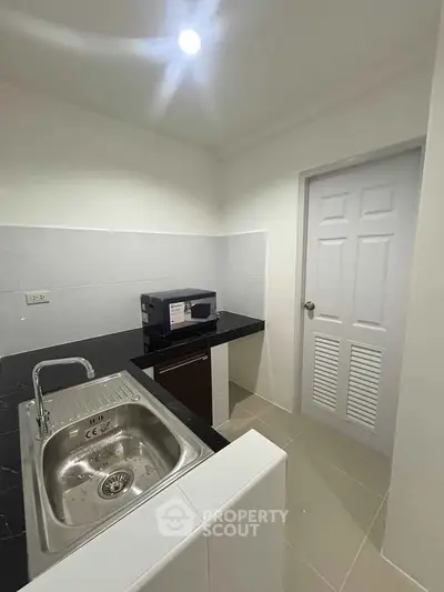 Modern kitchen with sleek black countertops and stainless steel sink, featuring a microwave and minimalist design.
